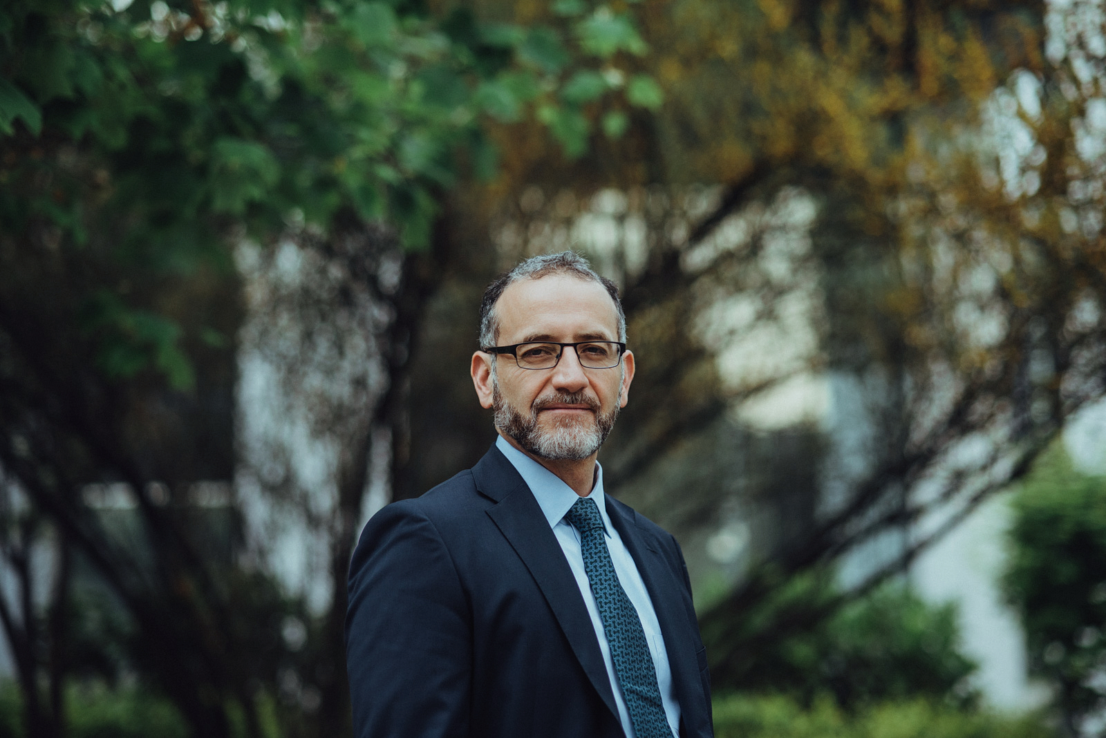 Retrato profesional en exterior de hombre con traje, fondo verde desenfocado y expresión natural